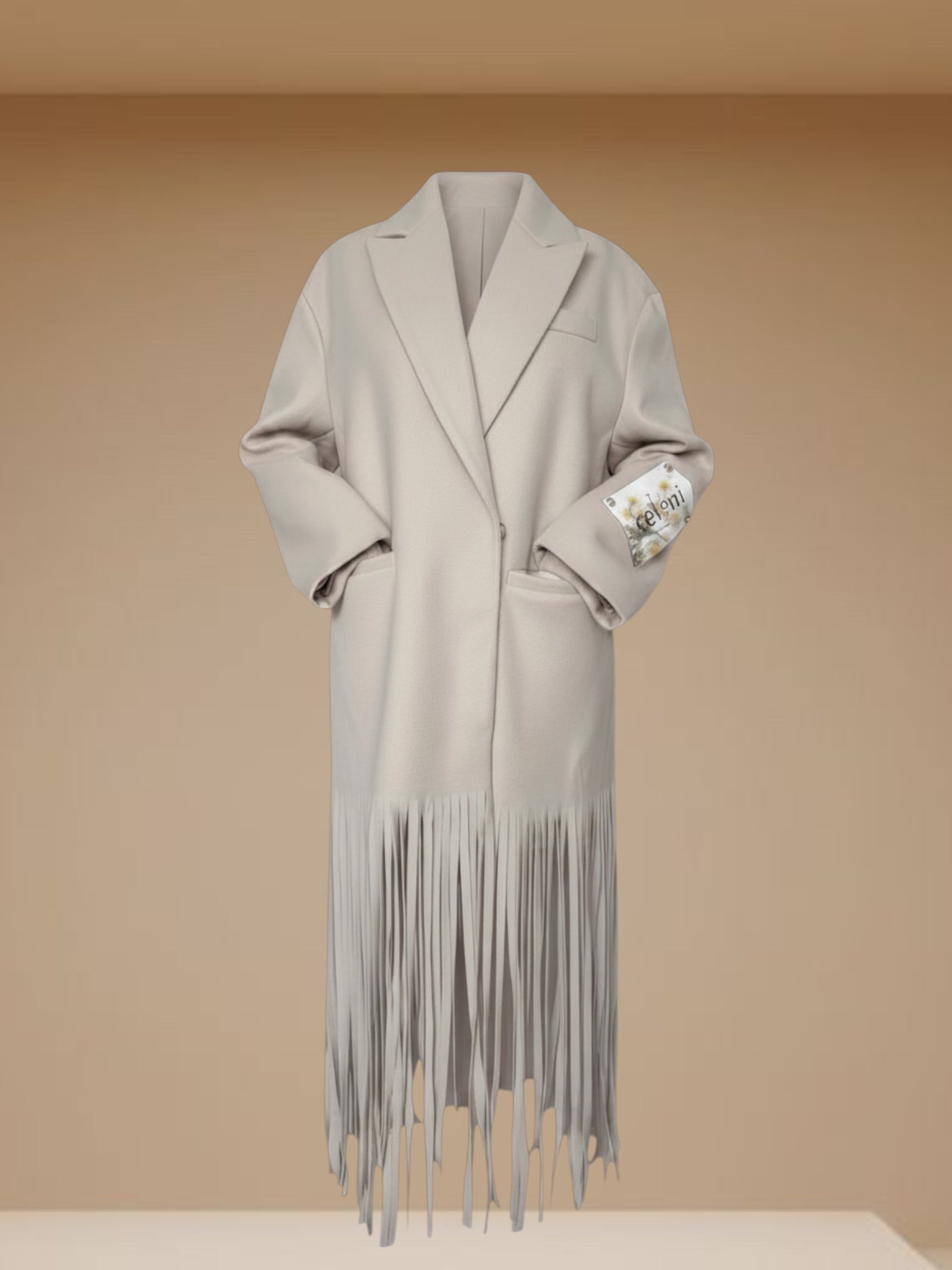 Celeni light beige oversized coat with fringe hem, notch lapels, and buttoned cross closure.